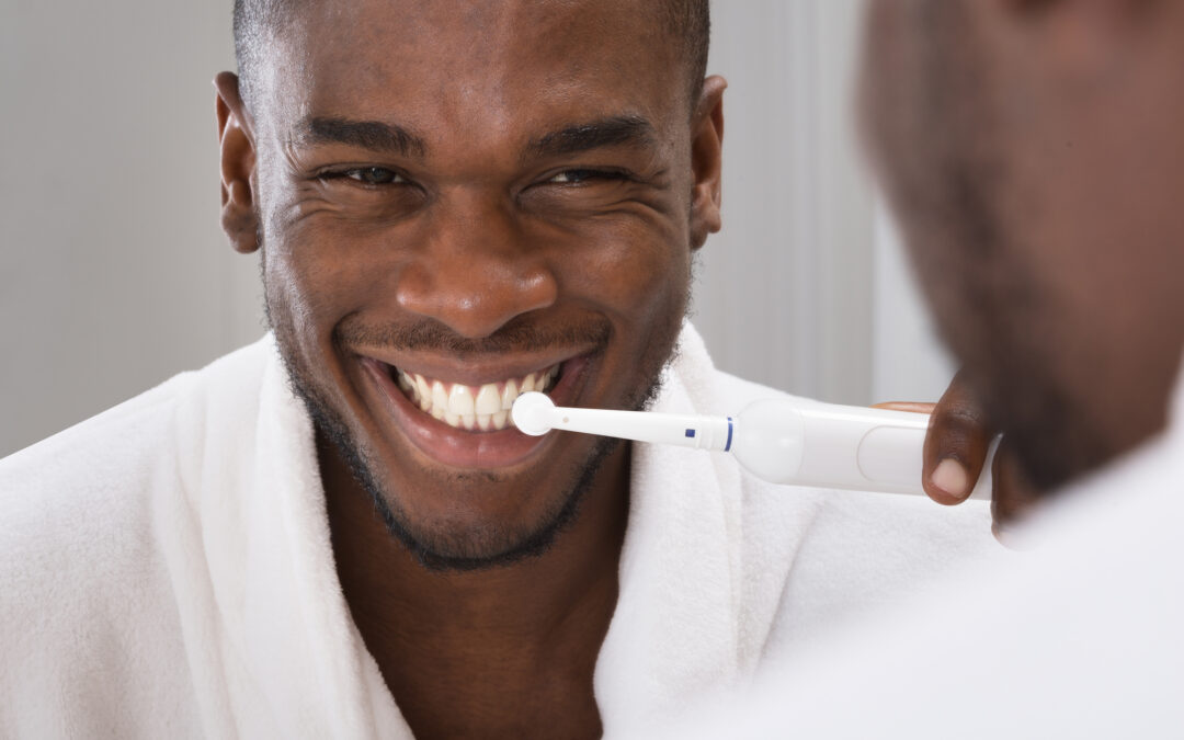 black man brushing with an electric toothbrush while looking in the mirror