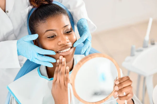 A patient sits in a dentist’s chair, looking in a mirror as her dentist shows the results of her new fillings. 