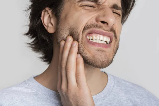 A man holds a hand to his jaw, grimacing with dental pain