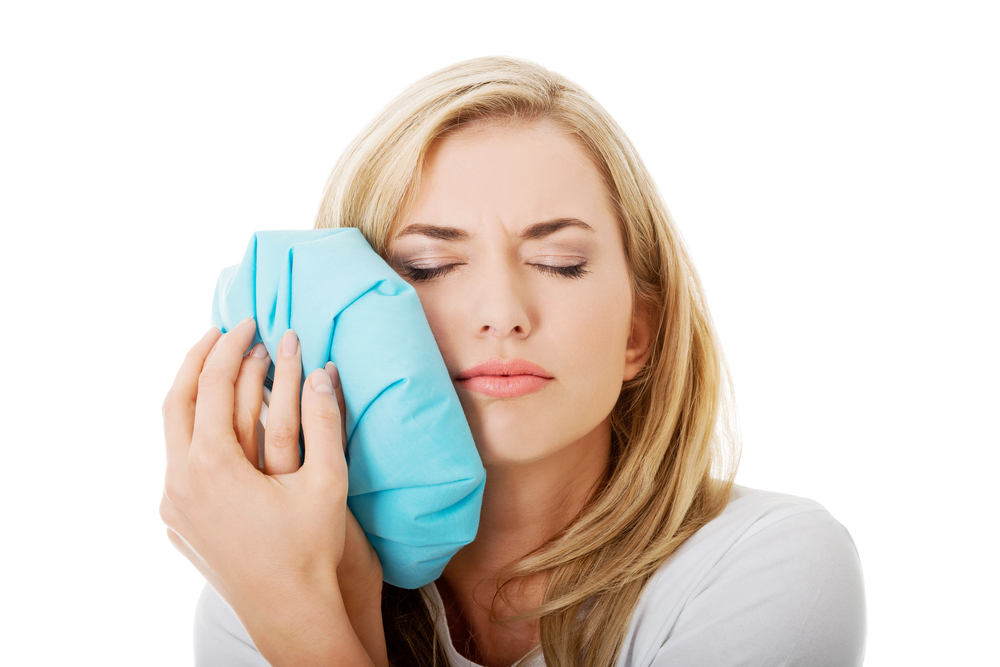 woman holding blue ice pack up to her face because of toothache, woman needs root canals