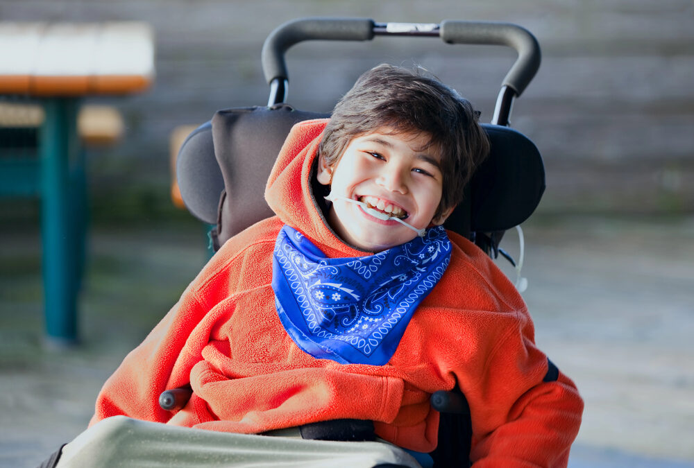 young boy with special needs in a wheel chair, wearing an orange hoodie and blue bandana around his neck