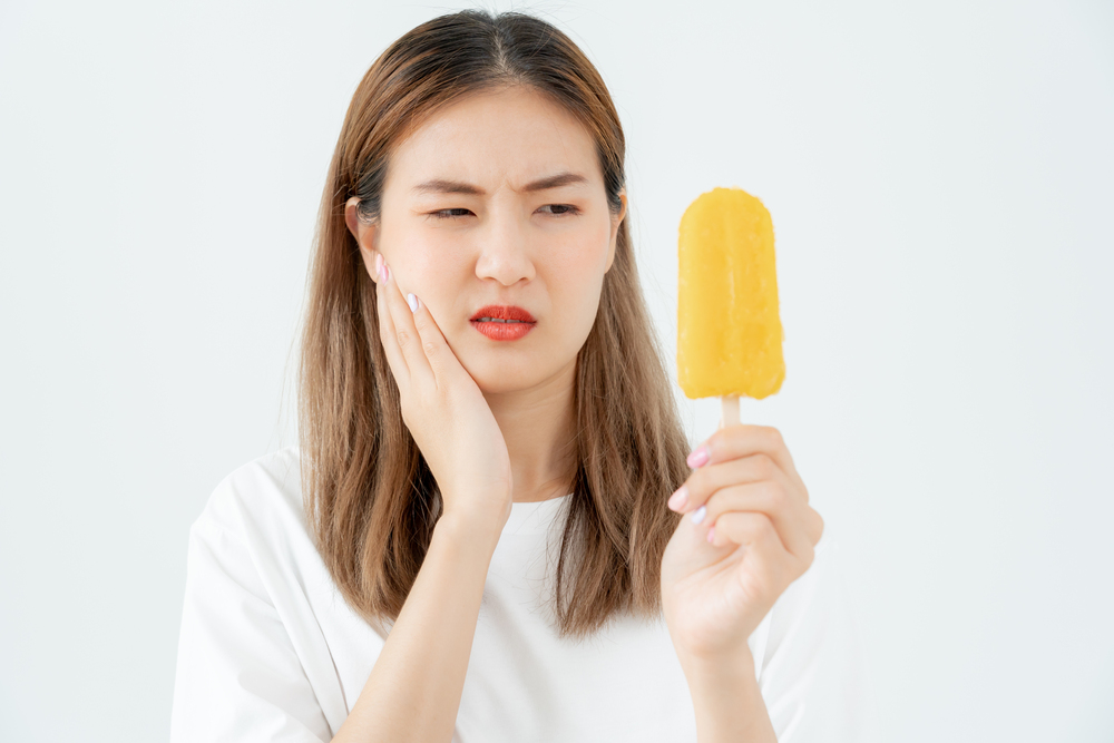 Asian woman feel sensitive teeth after eating ice cream, female suffer tooth sensitivity problems after teeth whitening